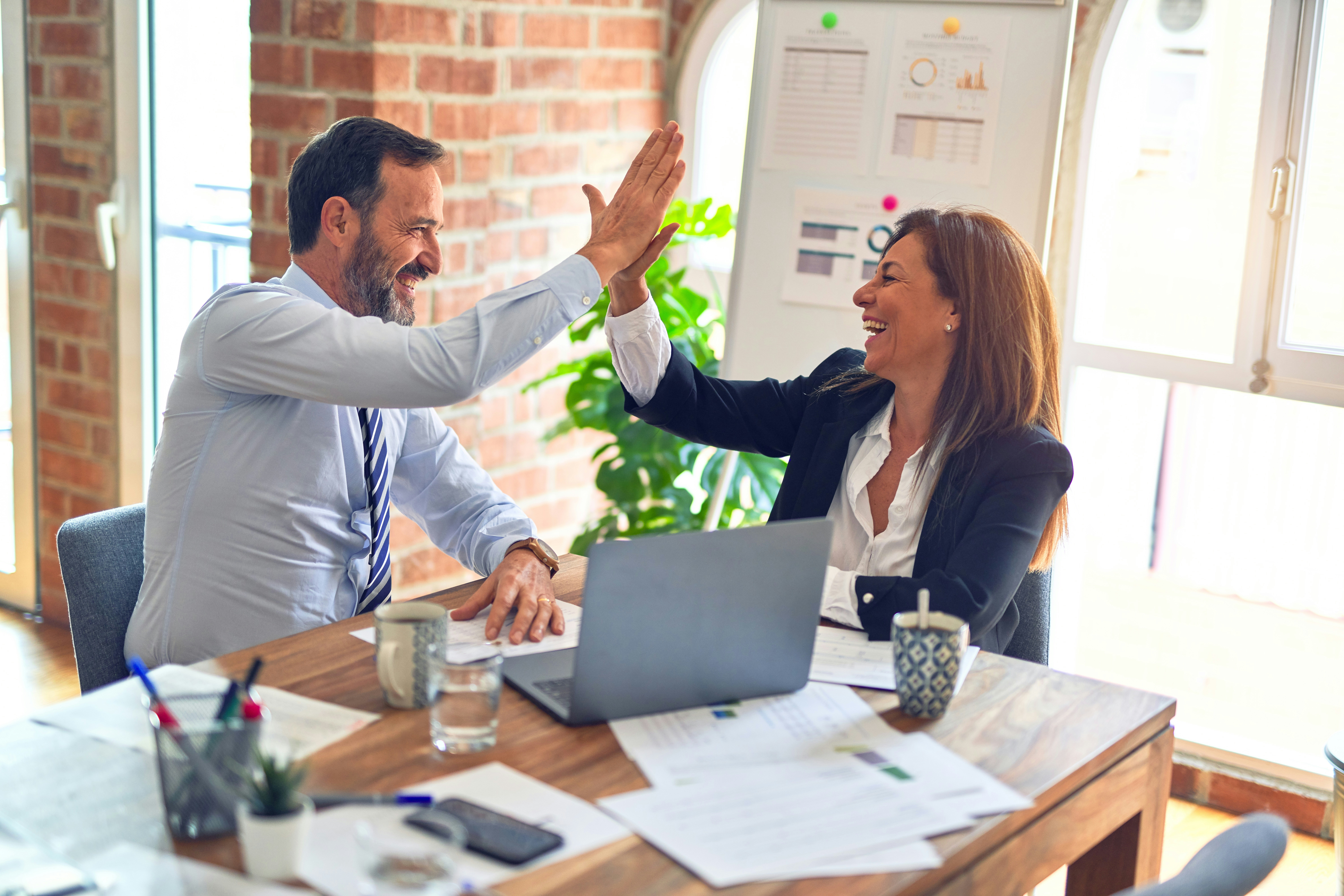 Two business professionals at a desk giving each other a high-five